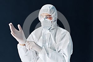 Doctor in protective medical suit puts on protective surgical sterile gloves on his arm