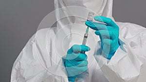 Doctor in protective PPE suit drawing Coronavirus Covid-19 vaccine bottle into syringe injection