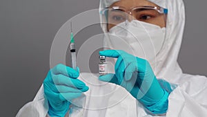 Doctor in protective PPE suit holding CoronavirusCovid-19 vaccine bottle and syringe injection