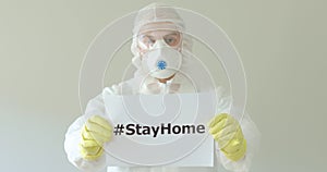 Doctor in protective suit holding hashtag stay at home in coronavirus pandemic.