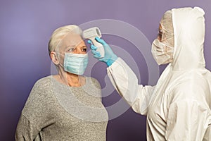 Doctor in protective suit taking temperature of an elderly lady