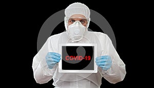 A doctor in the protective workwear display the digital tablet with message COVID-19