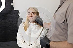 Doctor pulls female facial skin, lifting temple area, preparing to face reshape with