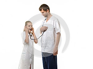 The doctor put the head of the phonendoscope to his heart, a girl in a medical coat listens with surprise to the doctor`s heart
