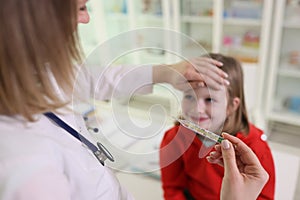 Doctor puts hand on forehead of girl looking at thermometer photo