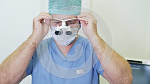 Doctor puts on magnifying binocular glasses and adjusts them, preparing for surgery in clinic