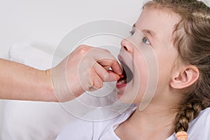 The doctor puts the pill in the little girl`s mouth, which opened