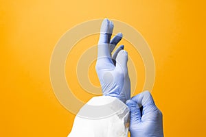 Doctor putting on blue latex medical gloves on yellow background Surgeon wearing gloves before surgery in operating room Infection