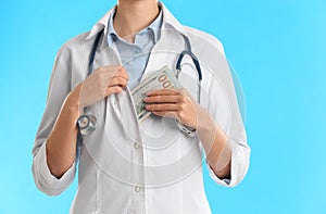 Doctor putting bribe money into pocket on blue background, closeup. Corruption in medicine