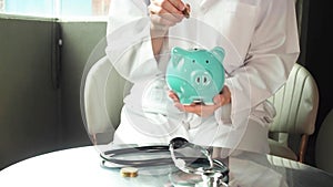 Doctor putting money into piggy bank, saving money for health, life insurance or healthcare concept. HD footage.