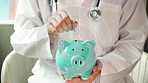 Doctor putting money into piggy bank, saving money for health, life insurance or healthcare concept. HD footage
