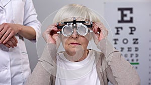 Doctor putting phoropter on elderly woman eyes, choosing proper lens diopter