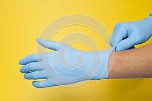 Doctor putting on protective blue gloves isolated on yellow background