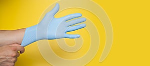 Doctor putting on protective blue gloves isolated on yellow background