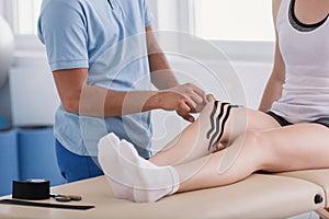 Doctor putting tapes on leg of sportswoman