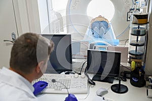 Doctor radiologist controls MRI or CT or PET Scan with female patient undergoing procedure