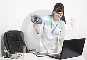 Doctor radiologist holds an x-ray picture of the tooth jaw and checks the data in a laptop, doctor`s office in the