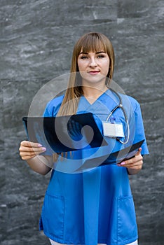 Doctor with x-ray. She`s holding it on grey background and examining