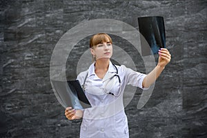 Doctor with x-ray. She`s holding it on grey background and examining