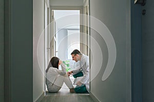 Doctor reassuring with empathy a patient sitting on the floor of a mental health center