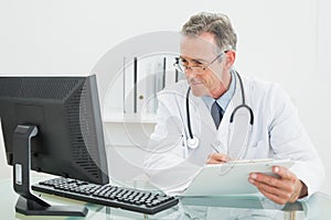 Doctor with report looking at computer monitor at medical office