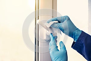 Doctor in rubber gloves disinfects window handles with sanitizer and napkins