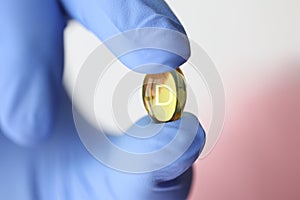 Doctor in rubber gloves holding vitamin D pill closeup