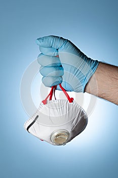 The doctor`s hand in a blue glove clutches a medical respirator, as a symbol of victory over the virus and the epidemic