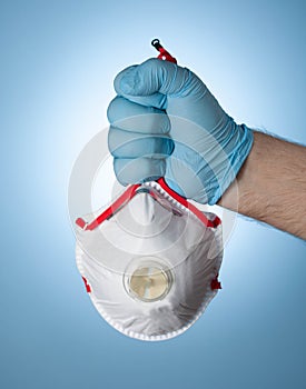 The doctor`s hand in a blue glove clutches a medical respirator, as a symbol of victory over the virus and the epidemic