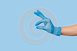 Doctor`s hand in a blue medical glove holds an object on a blue background. infection control. mocap, you can insert your product