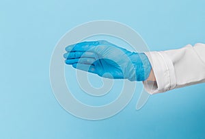 Doctor`s hand in a blue medical glove holds an object on a blue background. infection control. mocap, you can insert your product