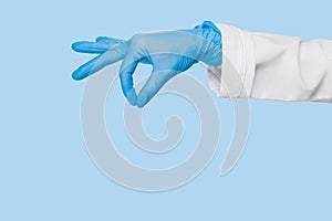 Doctor`s hand in a blue medical glove holds an object on a blue background. infection control. mocap, you can insert your product