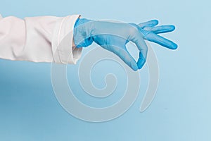 Doctor`s hand in a blue medical glove holds an object on a blue background. infection control. mocap, you can insert your product