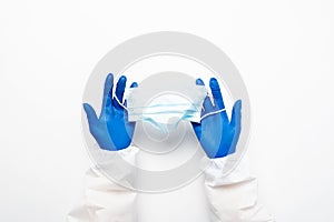 Doctor's hand in blue medical gloves holds anti-virus face mask on white background for pandemic, airborne diseases