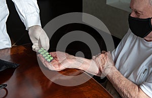 Doctor`s hand gives an old patient a pill. Gerontology service, nursing home. Unrecognizable people, part of the body