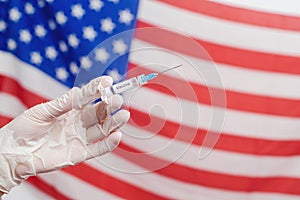 Doctor`s hand holding syringe with vaccine over United States of America flag background. USA Vaccination