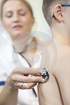 Doctor`s hand holds the stethoscope head attached to the back of the child during lung examination.