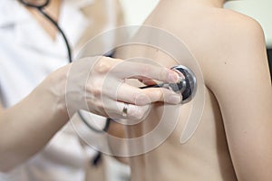 Doctor`s hand holds the stethoscope head attached to the back of the child during lung examination. photo