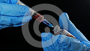 Doctor`s hand holds a syringe and a red vaccine bottle at the hospital on the black background. Health and medical