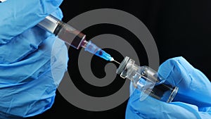 Doctor`s hand holds a syringe and a red vaccine bottle at the hospital on the black background. Health and medical