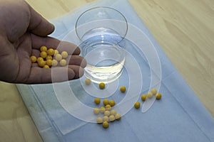 The doctor`s hand pours pills to a glass of water on a blue medical sheet