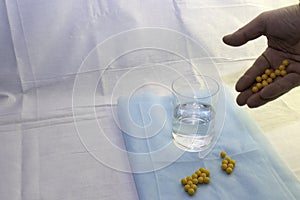 The doctor`s hand pours pills to a glass of water on a blue medical sheet