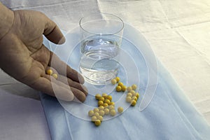 The doctor`s hand pours pills to a glass of water on a blue medical sheet