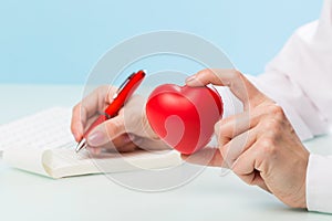 Doctor`s hand writes with pen on paper or notebook with a red heart on a blue background. medicine concept, modern technology,