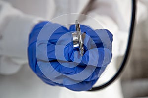 The doctor`s hands in blue gloves holding a stethoscope