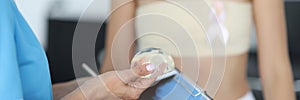 Doctor& x27;s hands are holding breast implant in front of clipboard with patient in background