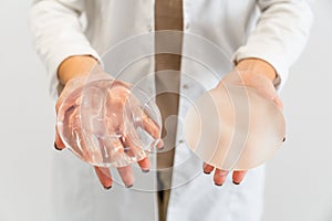 Doctor's hands holding two different types of breast prostheses.