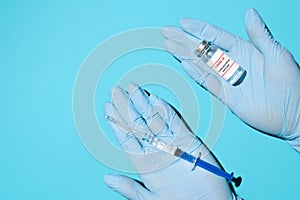 Doctor\'s hands in medical gloves holding a vial of vaccine and syringe, top view. Global population vaccination concept