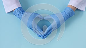 Doctor's hands in medical gloves making shape of heart on blue background with copy space.