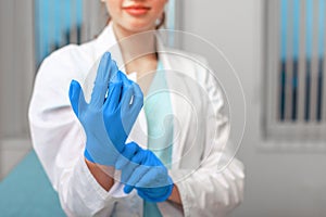 Doctor`s hands putting on latex gloves in a hospital. Woman in a doctor`s smock in latex gloves. Protection against